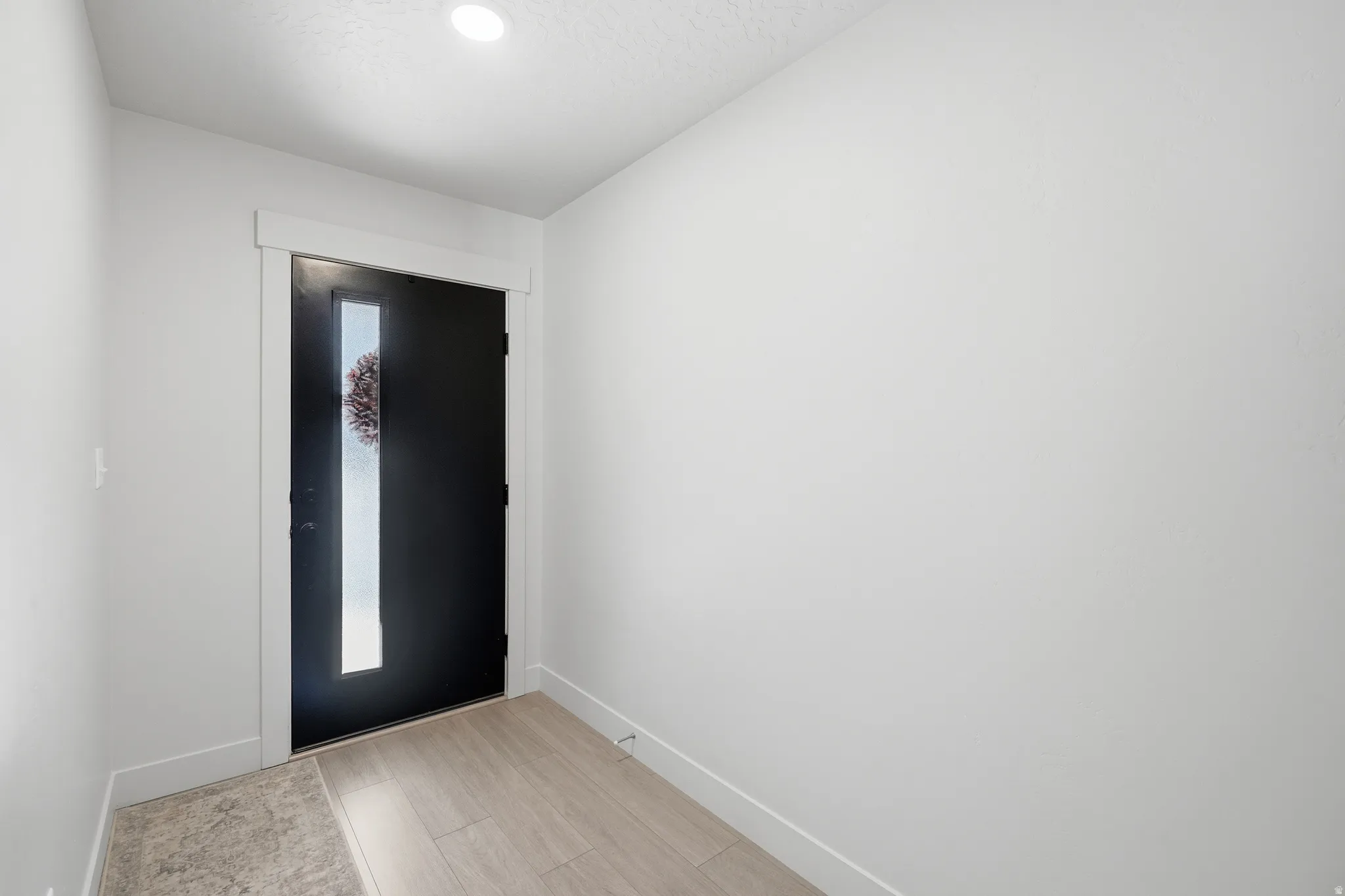 Entryway featuring a contemporary black door with a vertical frosted glass insert, neutral wall tones, recessed lighting, wood-finish flooring, and a coordinating tile landing