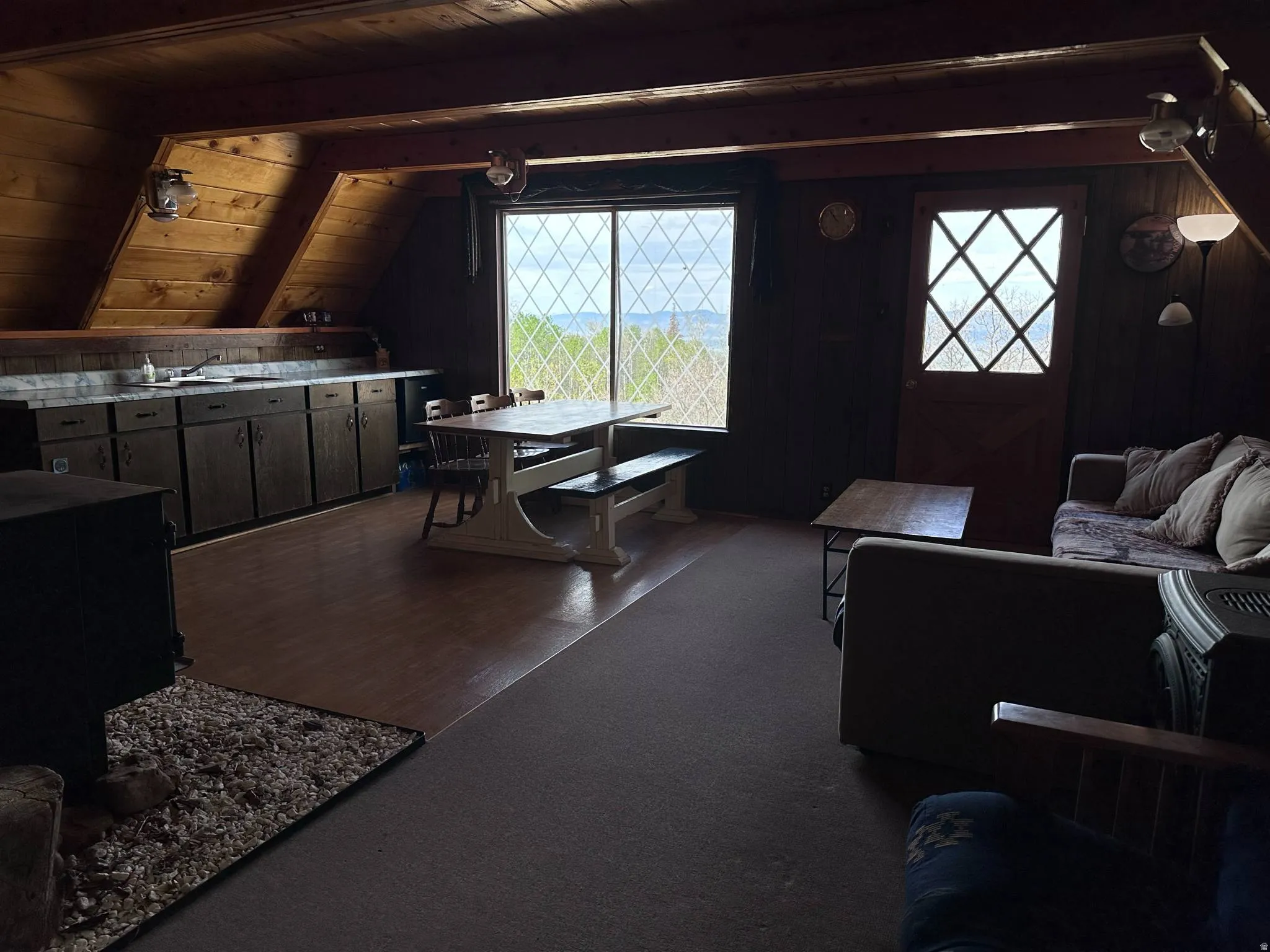 Interior space featuring a wood-paneled ceiling and walls, diamond-pane windows, wood-finish flooring, a built-in countertop with dark cabinetry, and a dark-paneled door with diamond-pane glass