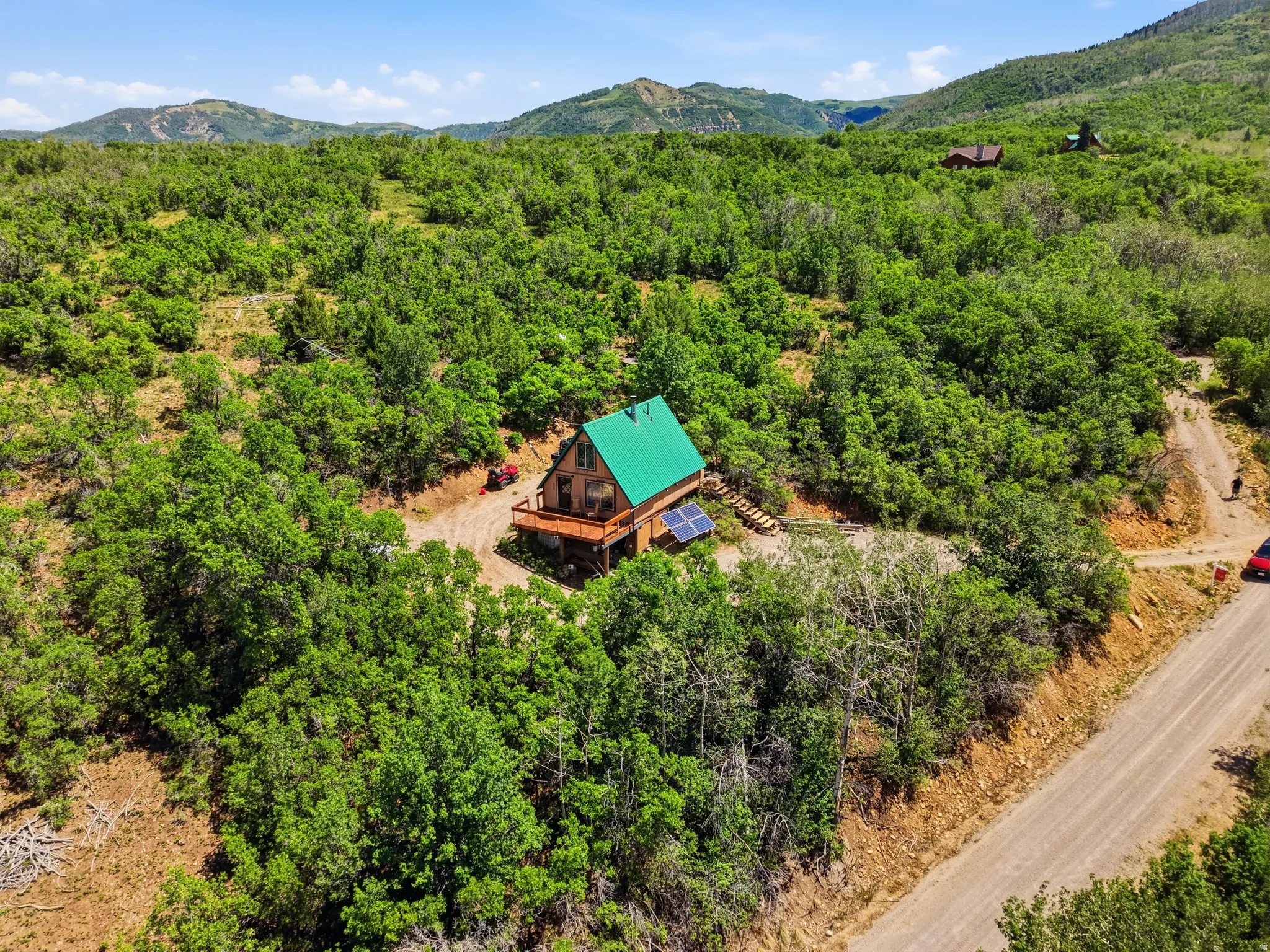 Wood-sided cabin featuring a green metal roof, a wrap-around wooden deck, and visible solar panels