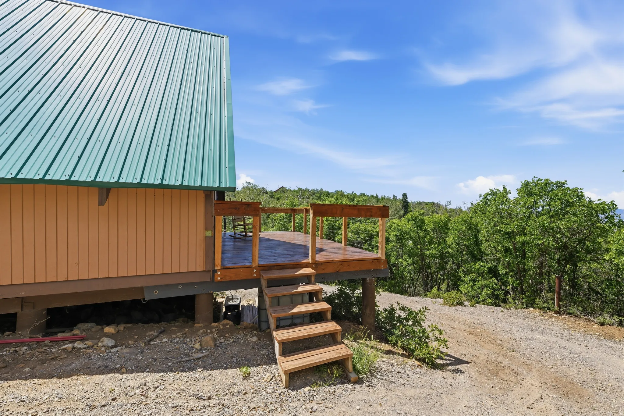 Exterior featuring a green metal roof, light brown siding, and a wooden deck with railing