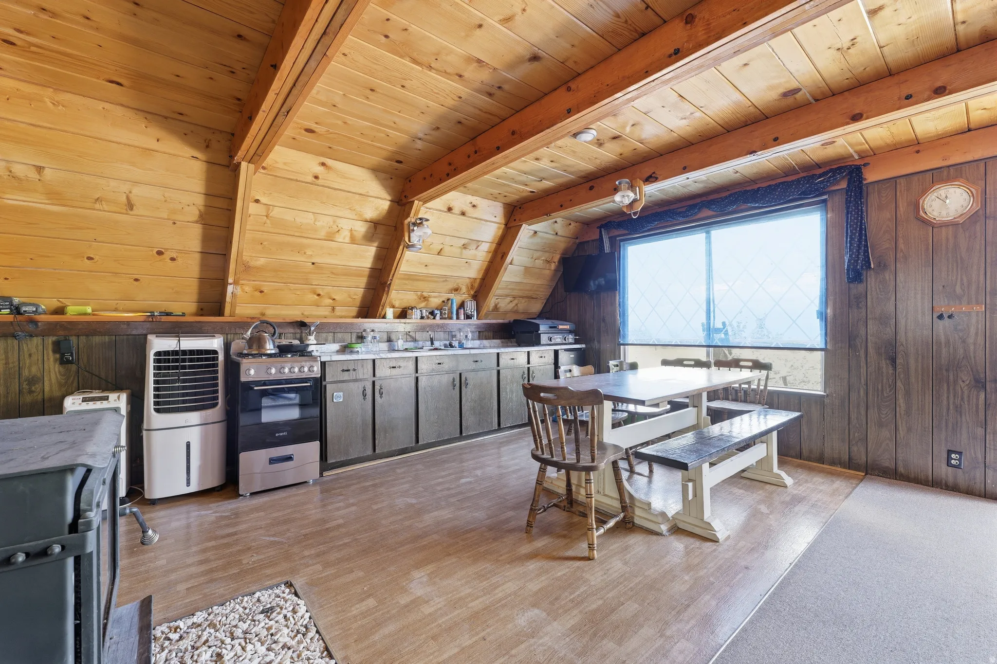 Wood-paneled kitchen and dining area featuring a full-size range, stainless steel sink, wood-finish flooring, and a large window