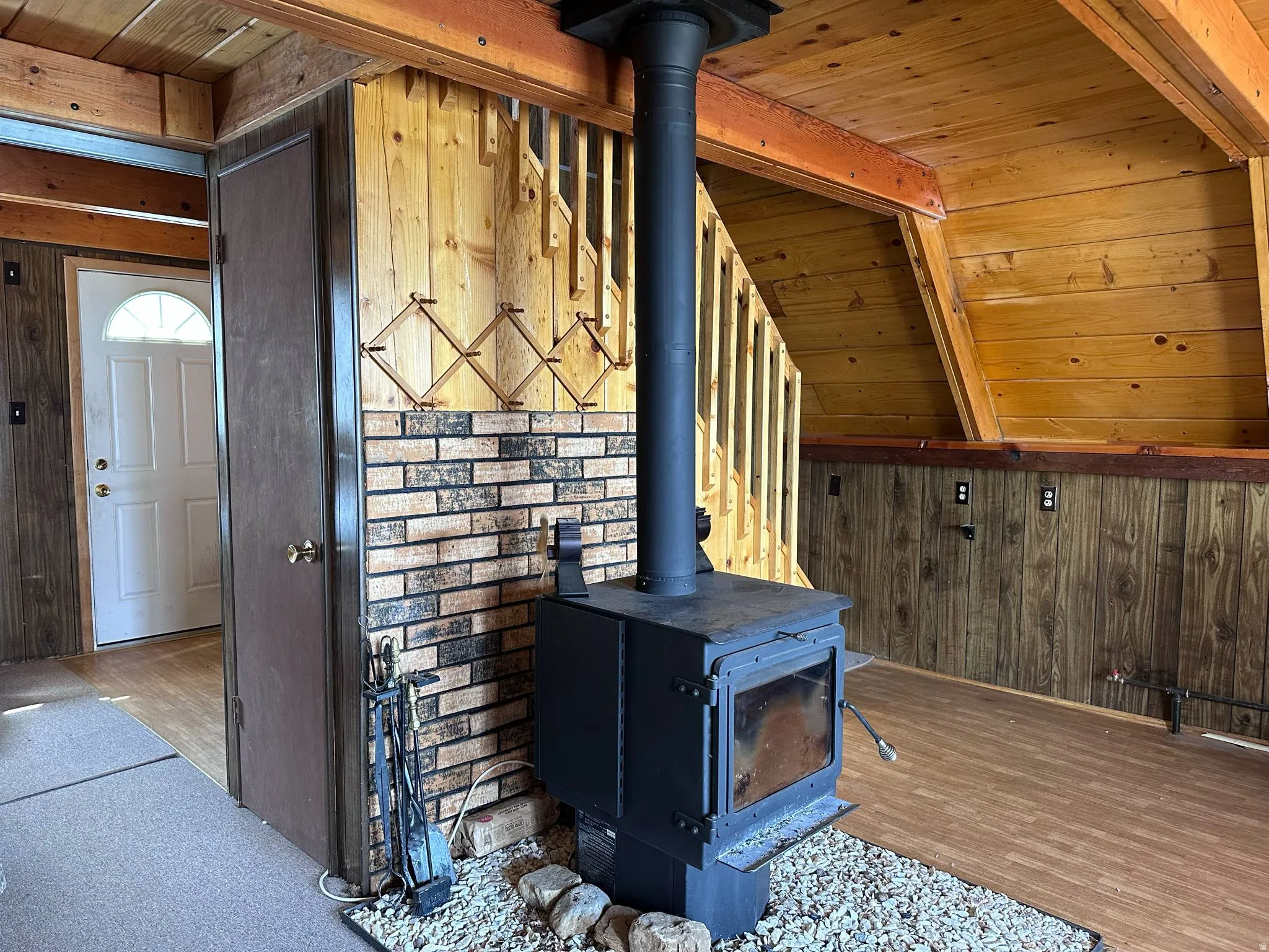 Wood-burning stove with a stone and brick surround, set against a backdrop of wood-paneled walls and a wood-finish floor