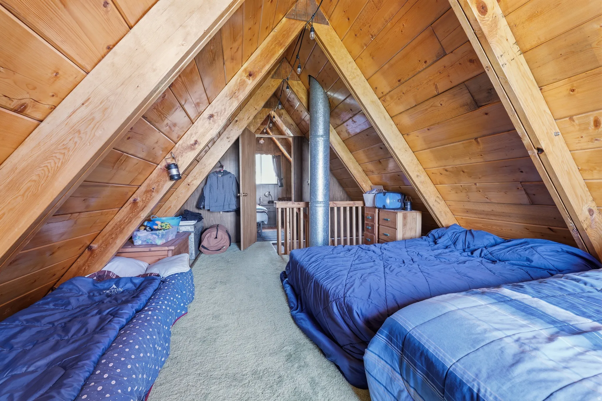 Attic space featuring wood-paneled walls, exposed wood ceiling beams, and light-colored carpeting