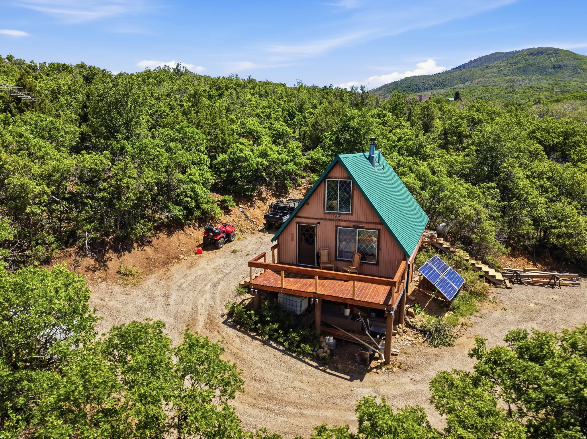A-frame cabin featuring a green metal roof, a wood deck, and exposed wood siding