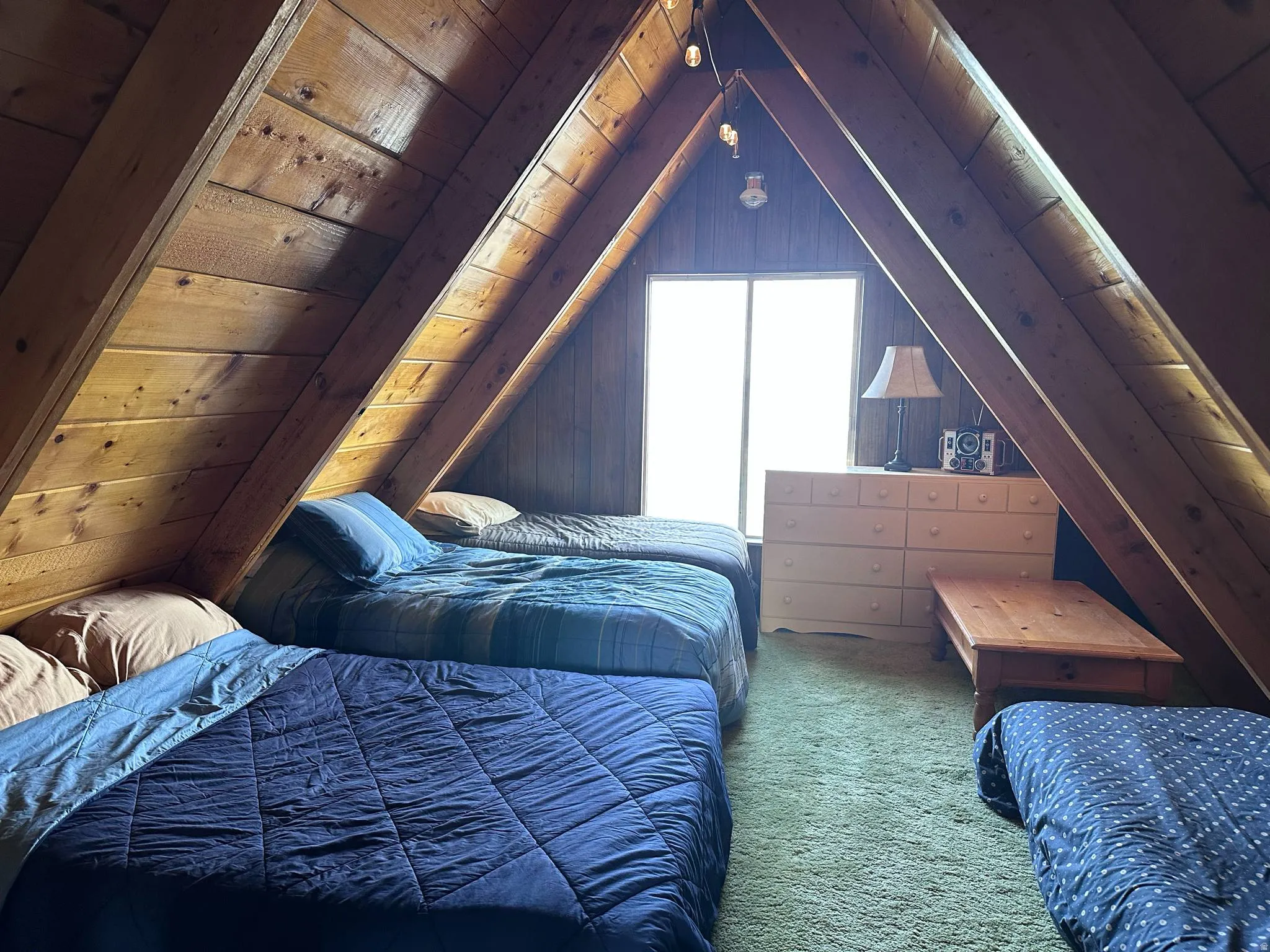 Vaulted attic space featuring exposed wood beams and paneling, a neutral carpeted floor, and a prominent window