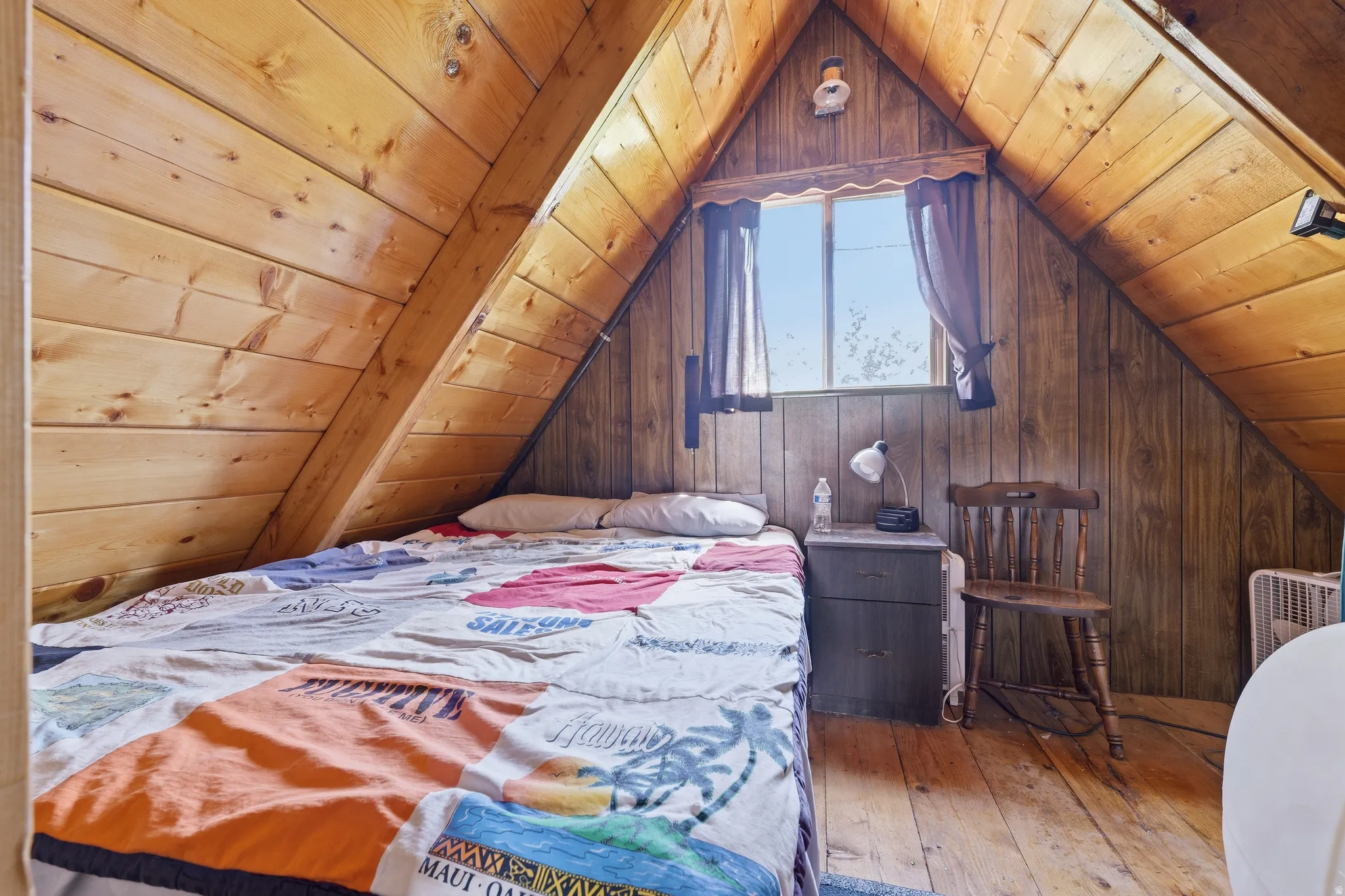 Sloped wood-paneled ceiling with exposed beams, wood-finish flooring, and a window with natural light
