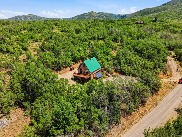 Wood-sided cabin featuring a green metal roof, a wrap-around wooden deck, and visible solar panels
