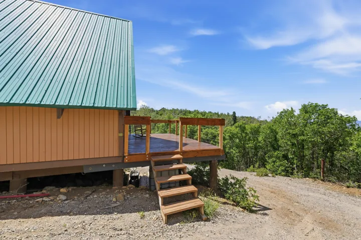 Exterior featuring a green metal roof, light brown siding, and a wooden deck with railing