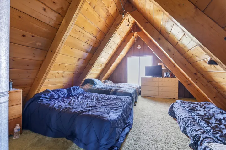 A-frame room with wood-paneled walls and ceiling, exposed wooden beams, and light-colored carpeting