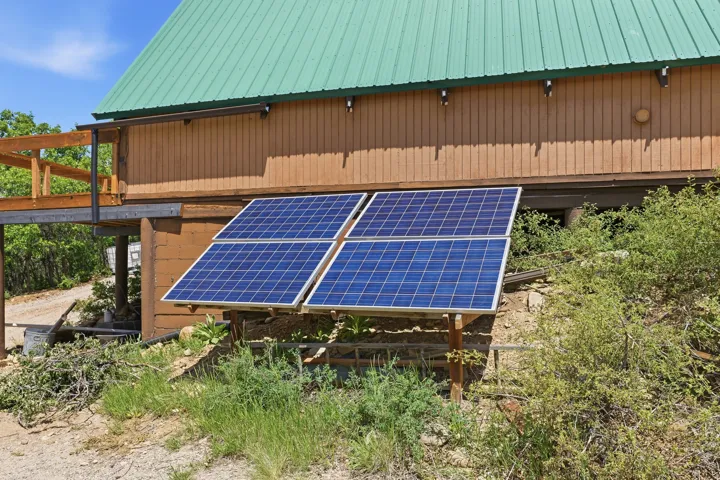 Exterior featuring four ground-mounted solar panels, wood-paneled siding, a green metal roof, and an elevated wood deck with railing