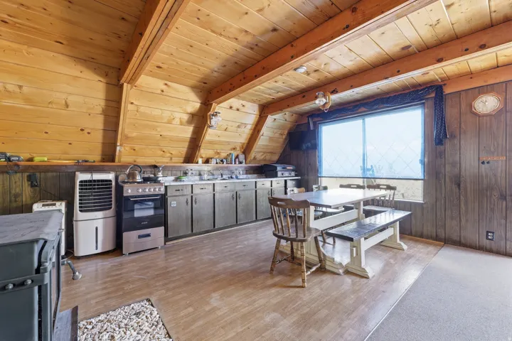 Wood-paneled kitchen and dining area featuring a full-size range, stainless steel sink, wood-finish flooring, and a large window
