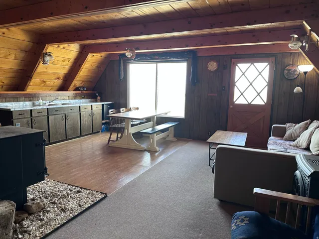 Open-concept living space with wood-paneled walls and ceiling, featuring a wood-burning stove with a stone and wood chip hearth
