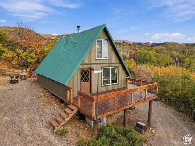 A-frame cabin featuring a green metal roof, multiple windows, and a raised wood-finish deck with railing