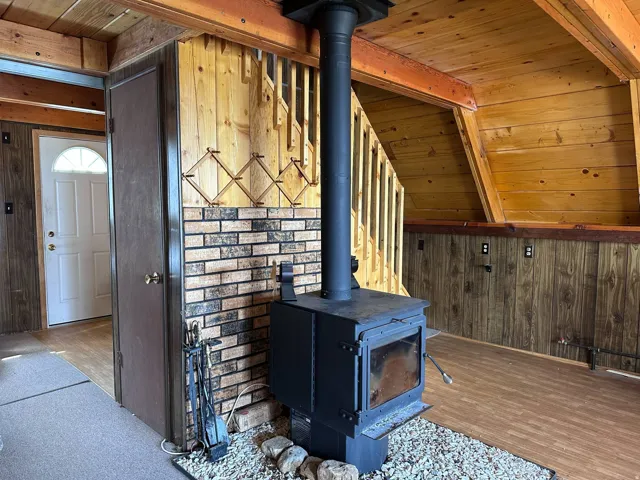 Wood-burning stove with a stone and brick surround, set against a backdrop of wood-paneled walls and a wood-finish floor