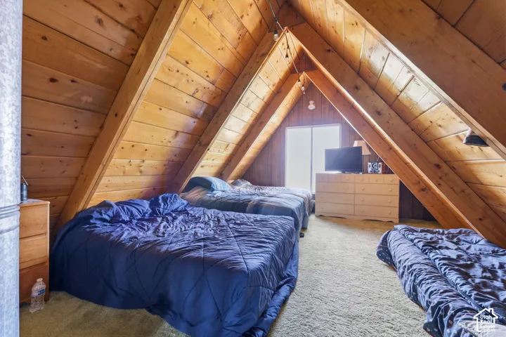 A-frame room with wood-paneled walls and ceiling, exposed wooden beams, and light-colored carpeting