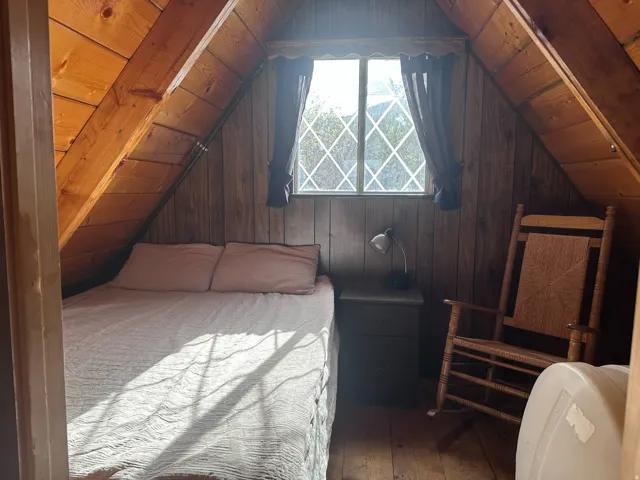 Attic space featuring paneled wood walls, exposed wood beams, diamond-paned window, and wood-finish flooring