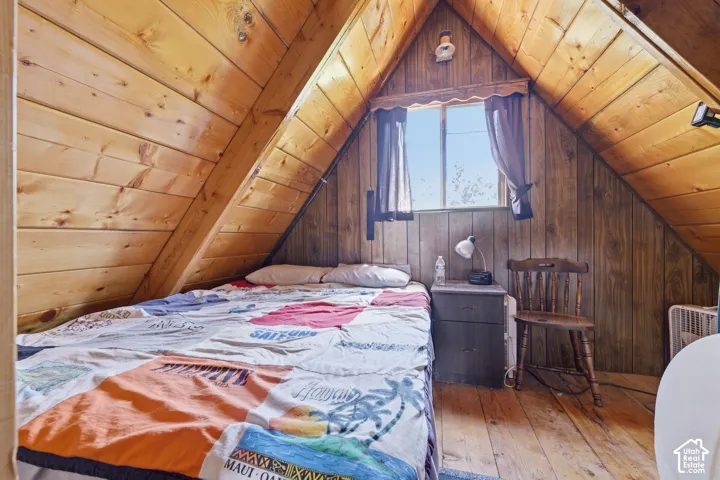 Sloped wood-paneled ceiling with exposed beams, wood-finish flooring, and a window with natural light