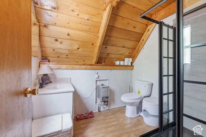 Bathroom featuring wood-finish flooring, white paneling, and a natural wood planked sloped ceiling