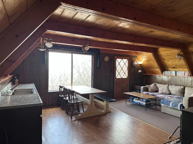 Open-concept living area featuring wood-finish flooring, exposed wood beam ceiling, and paneled walls