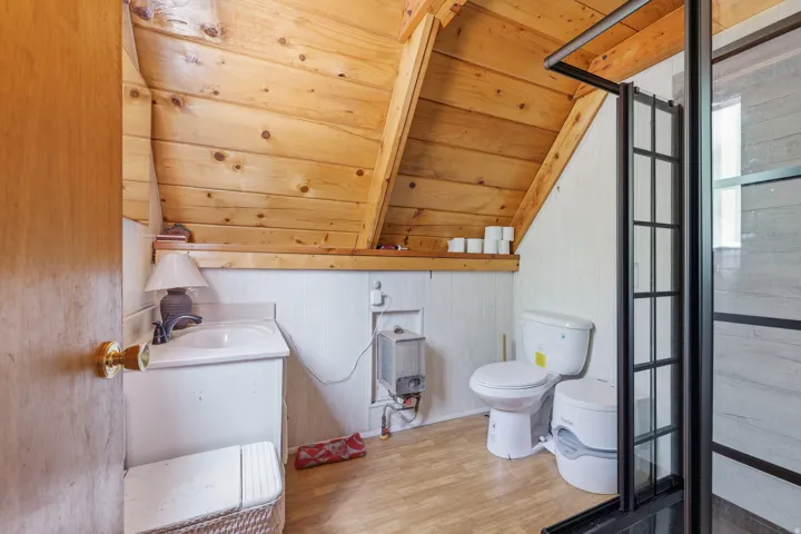 Bathroom featuring wood-finish flooring, white paneling, and a natural wood planked sloped ceiling