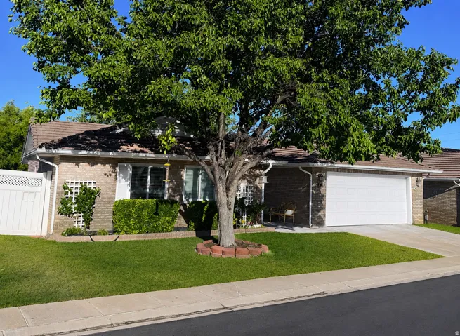 Traditional brick exterior featuring a front-facing attached garage, concrete driveway, and a manicured lawn with mature tree
