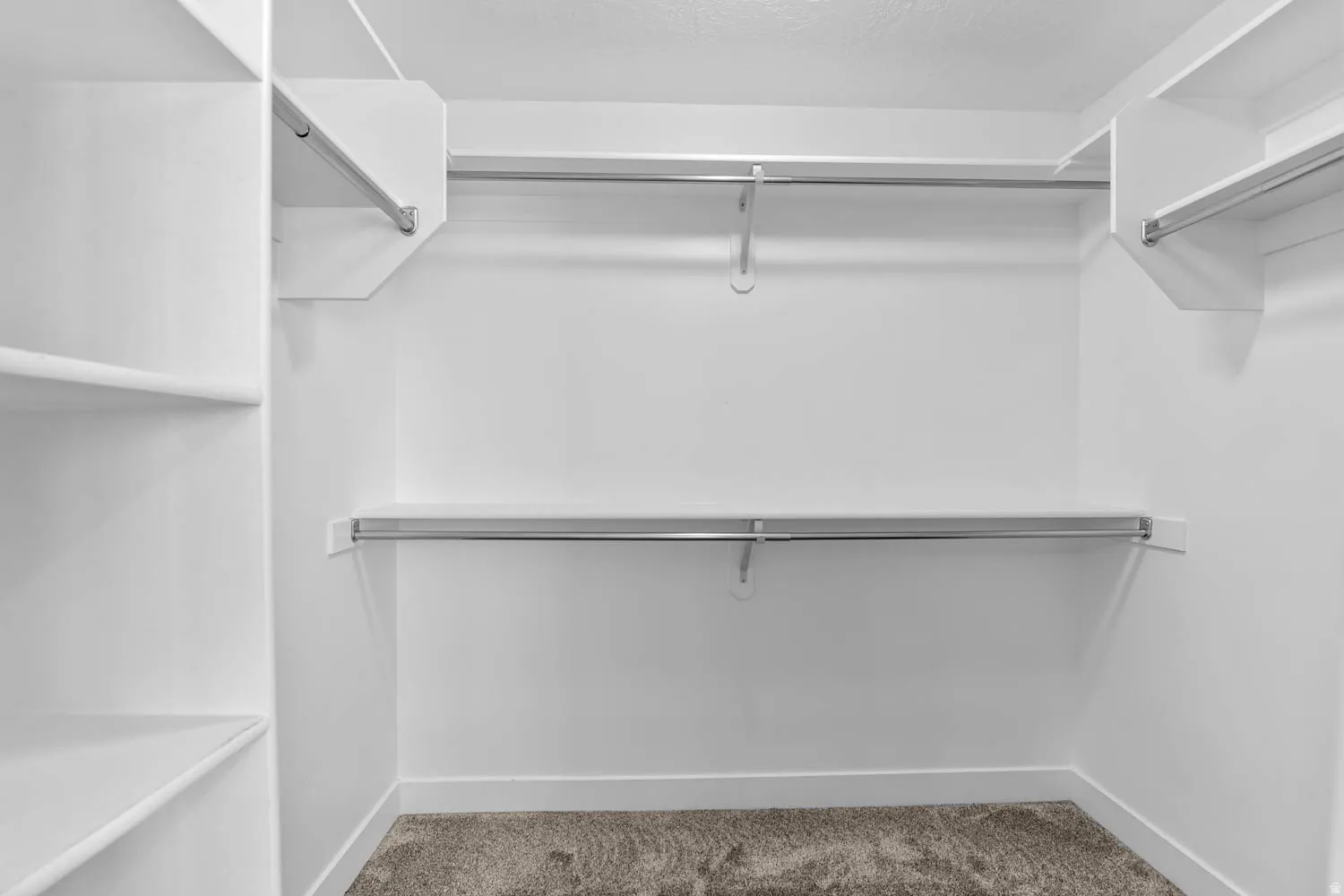 Walk-in closet featuring white built-in shelving, multiple hanging rods, white walls, white baseboards, and carpet flooring