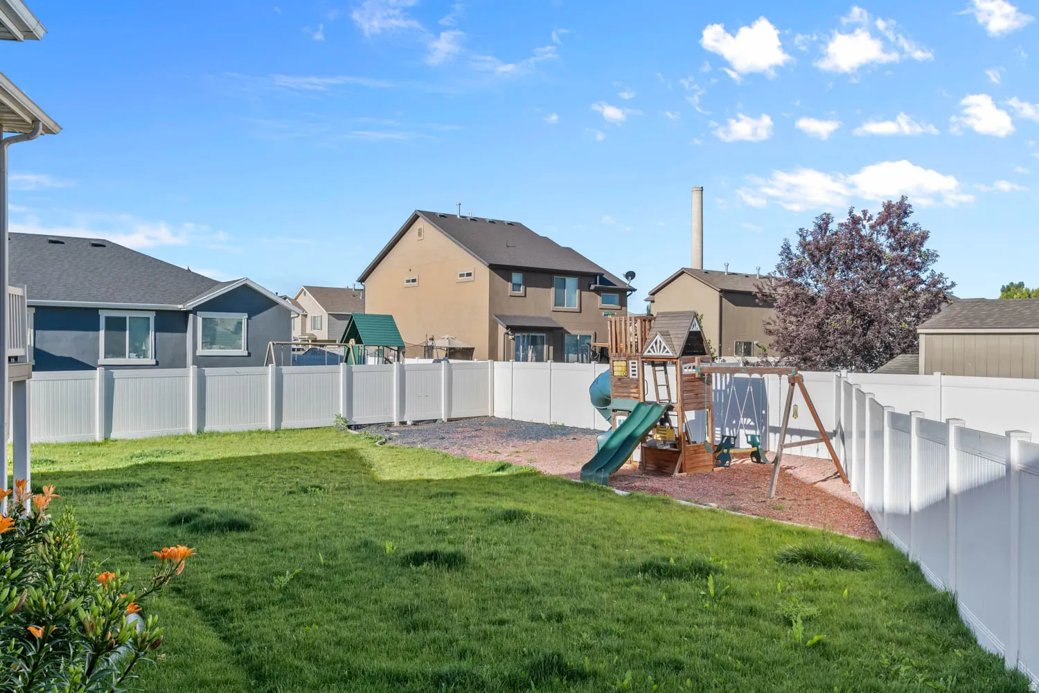Spacious backyard featuring a manicured lawn, white privacy fencing, and an established play structure with a slide and swings