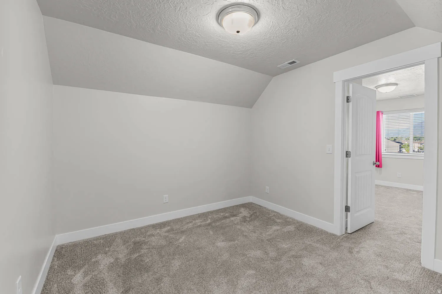 Carpeted room featuring a sloped ceiling and flush-mount lighting