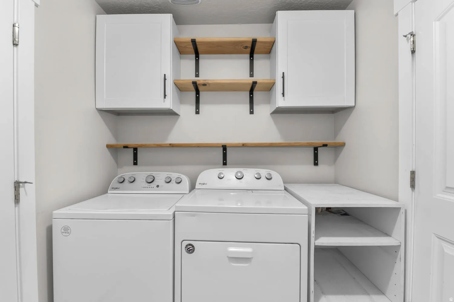 Dedicated laundry area featuring a built-in folding counter, white cabinetry, and natural wood-finish shelving with black brackets