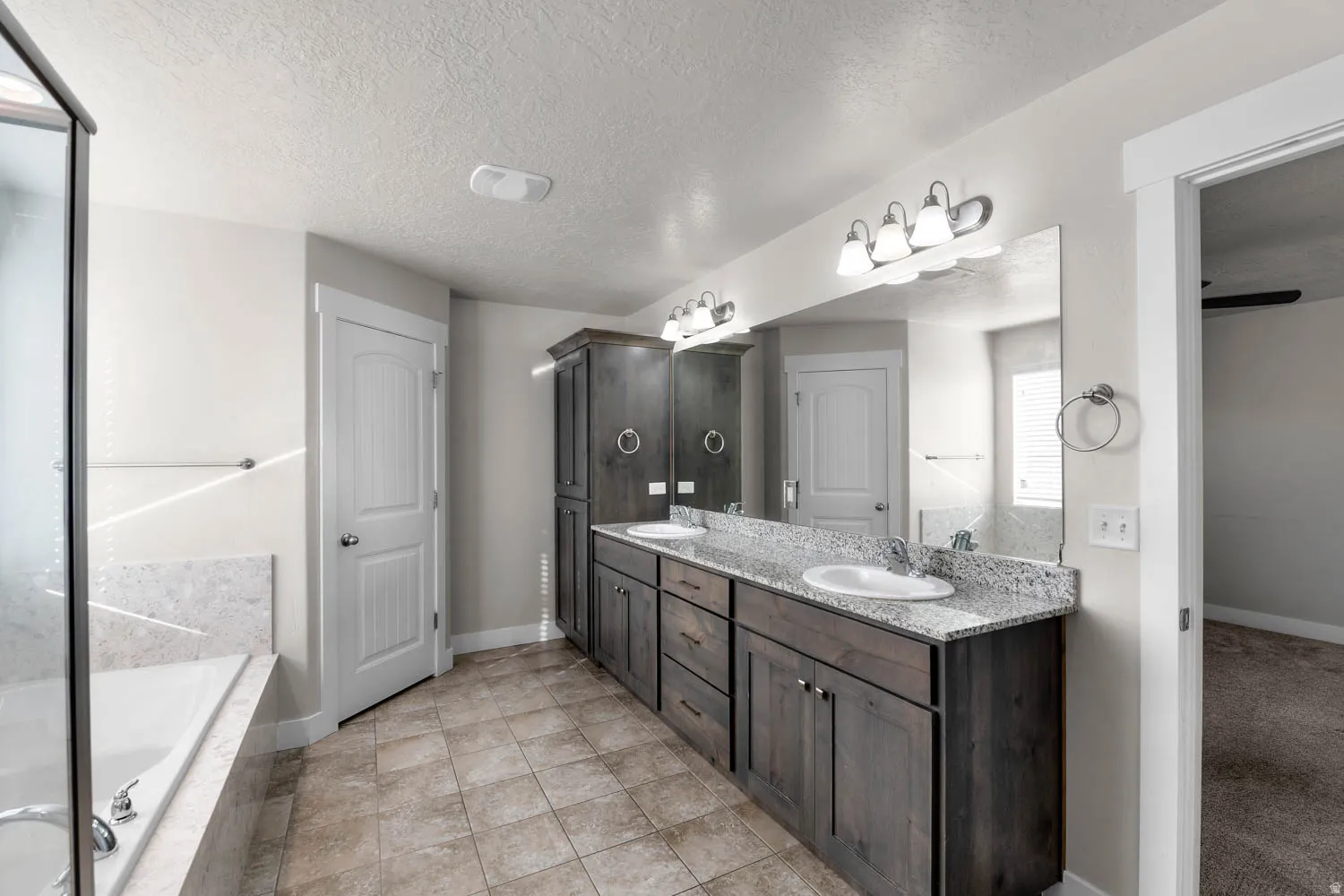Bathroom featuring a double vanity with granite-style countertops, integrated sinks, dark wood-finish cabinetry, and a large wall-mounted mirror