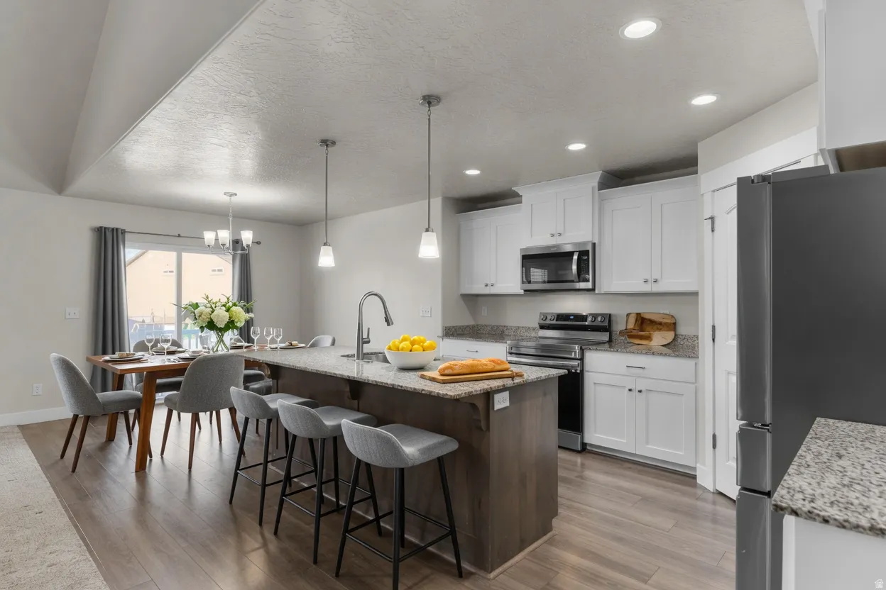 Open-concept kitchen and dining area featuring wood-finish flooring, white cabinetry, stainless steel appliances, granite countertops, and recessed lighting