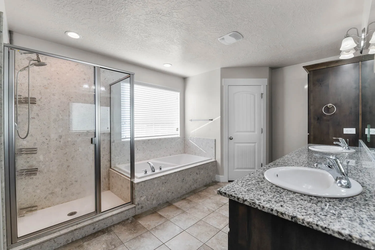 Bathroom featuring a glass-enclosed shower with a rainfall showerhead, a separate soaking tub, and a dual vanity with a granite-style countertop