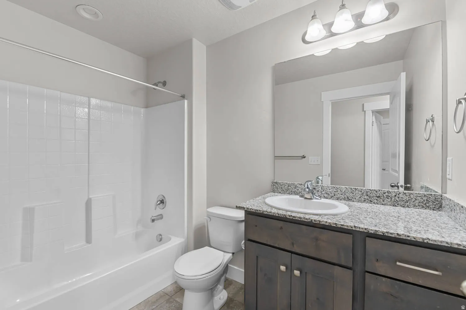 Bathroom featuring a dark wood-finish vanity with a light speckled countertop, an undermount sink, and a chrome faucet