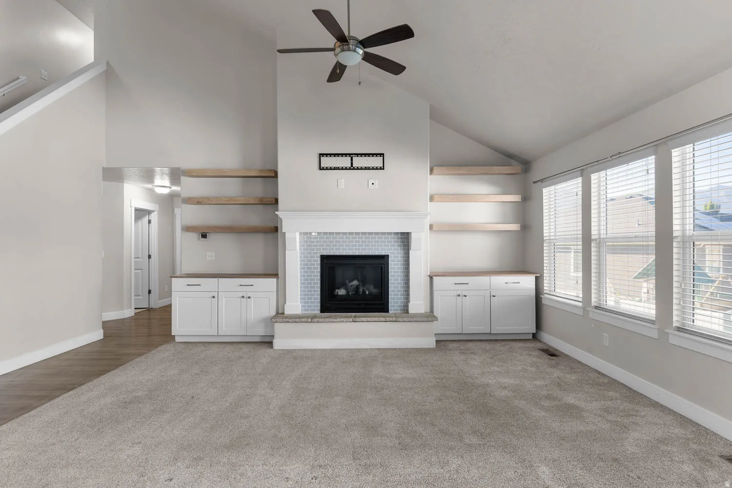 Spacious living area featuring vaulted ceilings, a central fireplace with a tiled surround, built-in cabinetry with natural wood shelves, and multiple large windows