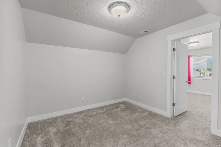 Carpeted room featuring a sloped ceiling and flush-mount lighting