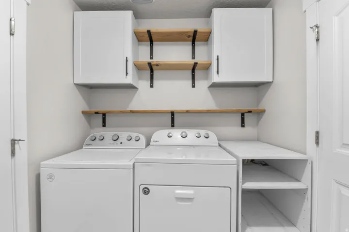 Dedicated laundry area featuring a built-in folding counter, white cabinetry, and natural wood-finish shelving with black brackets