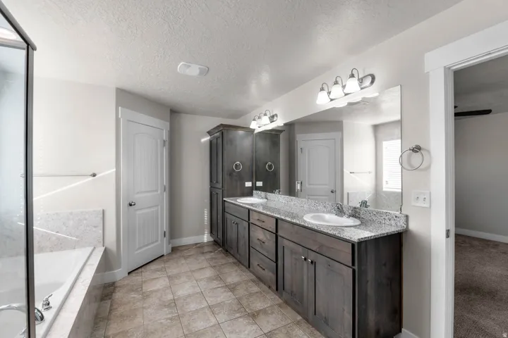 Bathroom featuring a double vanity with granite-style countertops, integrated sinks, dark wood-finish cabinetry, and a large wall-mounted mirror