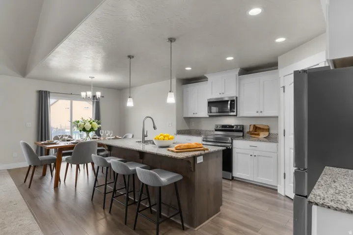 Open-concept kitchen and dining area featuring wood-finish flooring, white cabinetry, stainless steel appliances, granite countertops, and recessed lighting