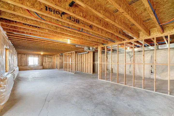 Unfinished basement featuring exposed wood joists, concrete flooring, and framed interior walls