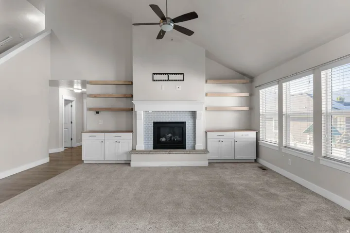 Spacious living area featuring vaulted ceilings, a central fireplace with a tiled surround, built-in cabinetry with natural wood shelves, and multiple large windows