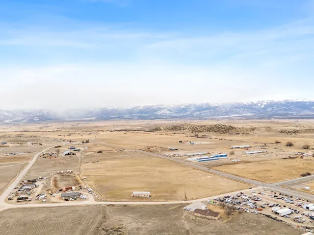 Expansive land featuring multiple structures, paved road access, and distant snow-capped mountains
