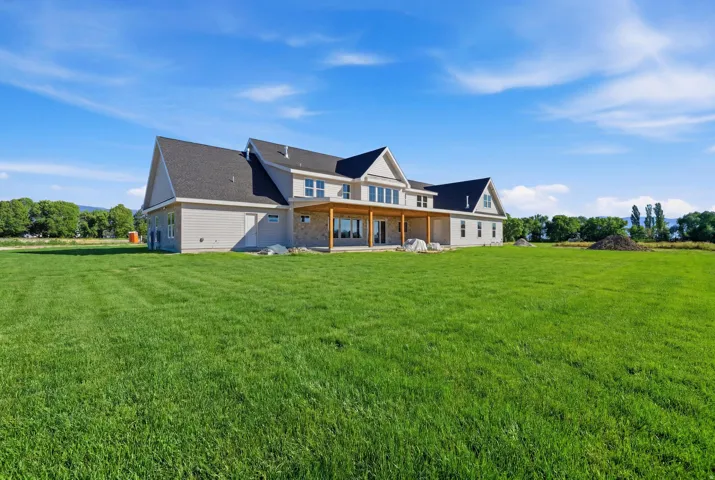 Expansive green lawn surrounds a newly constructed residence featuring light-colored siding, a dark shingle roof, and a covered back patio with natural wood posts