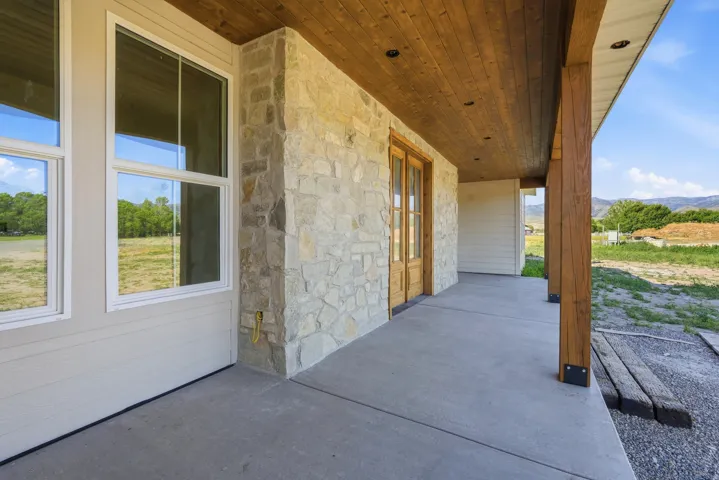 Expansive covered porch featuring a natural wood-finish ceiling, exposed structural beams, and stone veneer accents