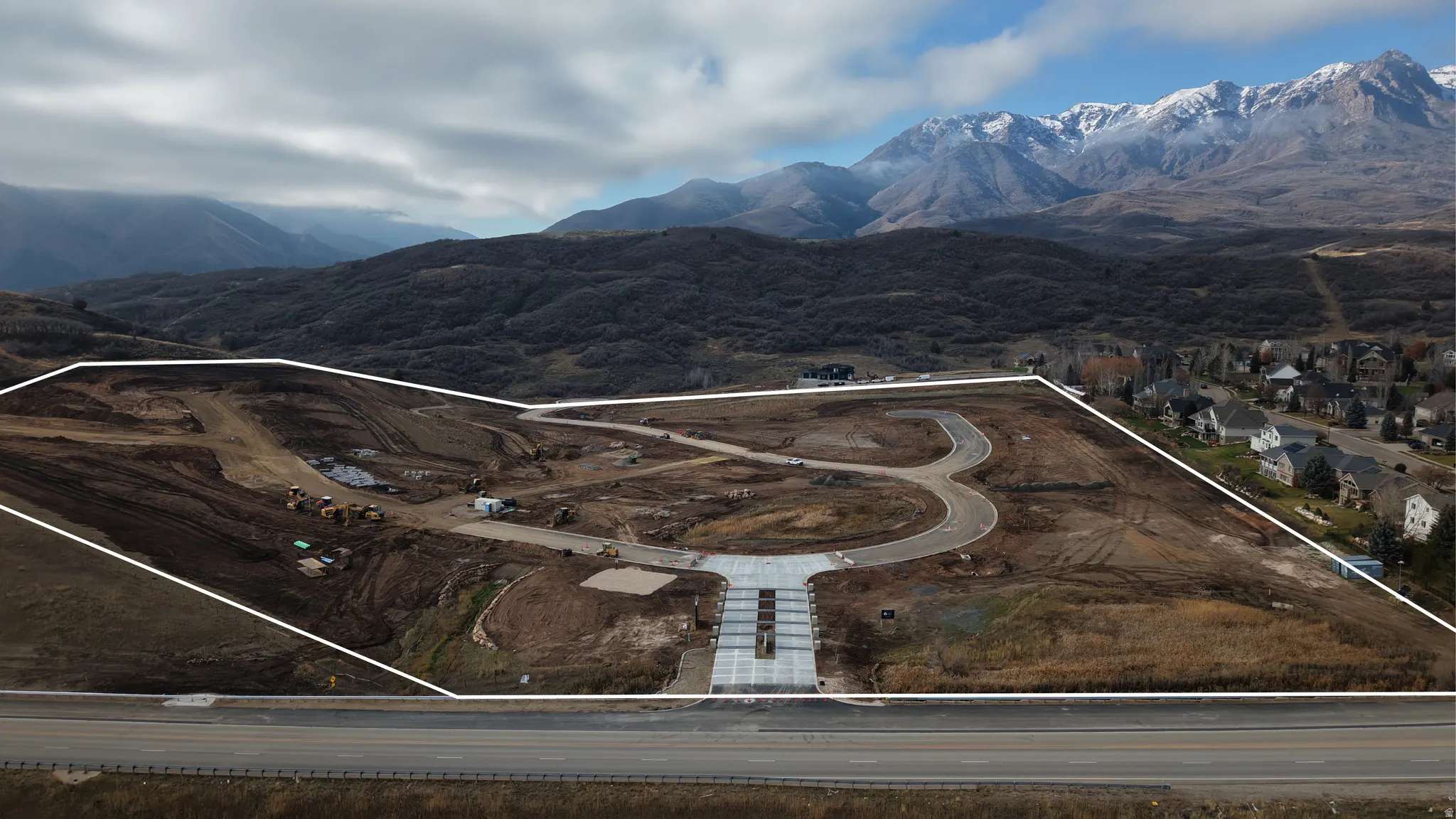 Expansive land parcel featuring partial road infrastructure, mountain backdrop, and proximity to established residential properties