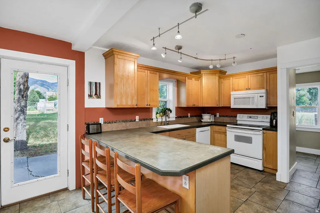 Kitchen featuring wood cabinetry, white appliances, track lighting, and a kitchen island with seating