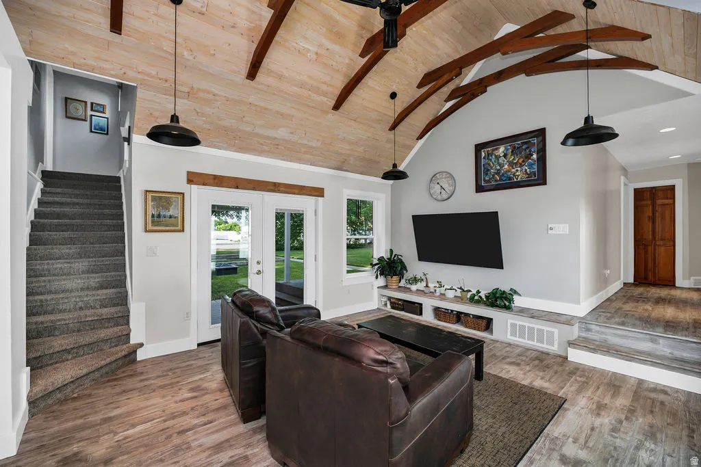 Vaulted wood-paneled ceiling with exposed wood beams, featuring wood-finish flooring, a built-in media console, and a carpeted staircase