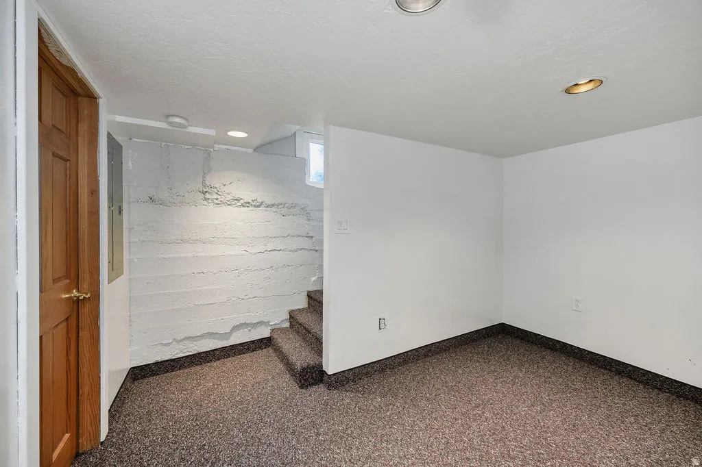 Finished basement room featuring textured concrete walls, recessed lighting, and multi-tone carpet flooring
