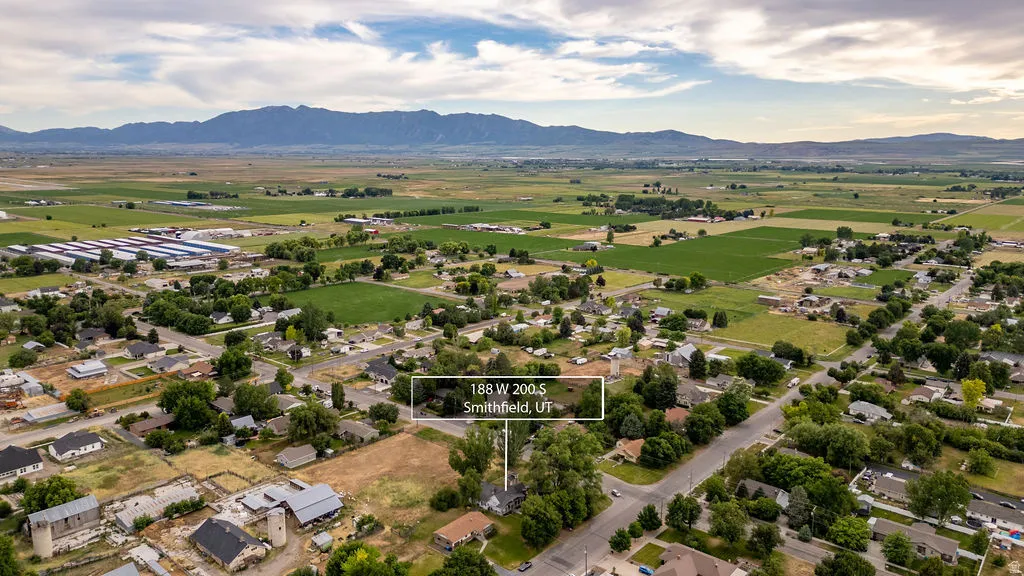 Aerial perspective showcasing a residential property within a broader community, bordered by agricultural fields and distant mountains