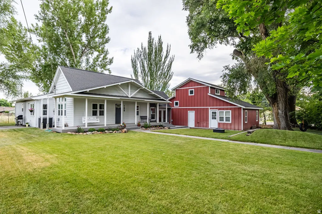 Spacious property featuring a light gray residence with a covered front porch and a separate red barn structure