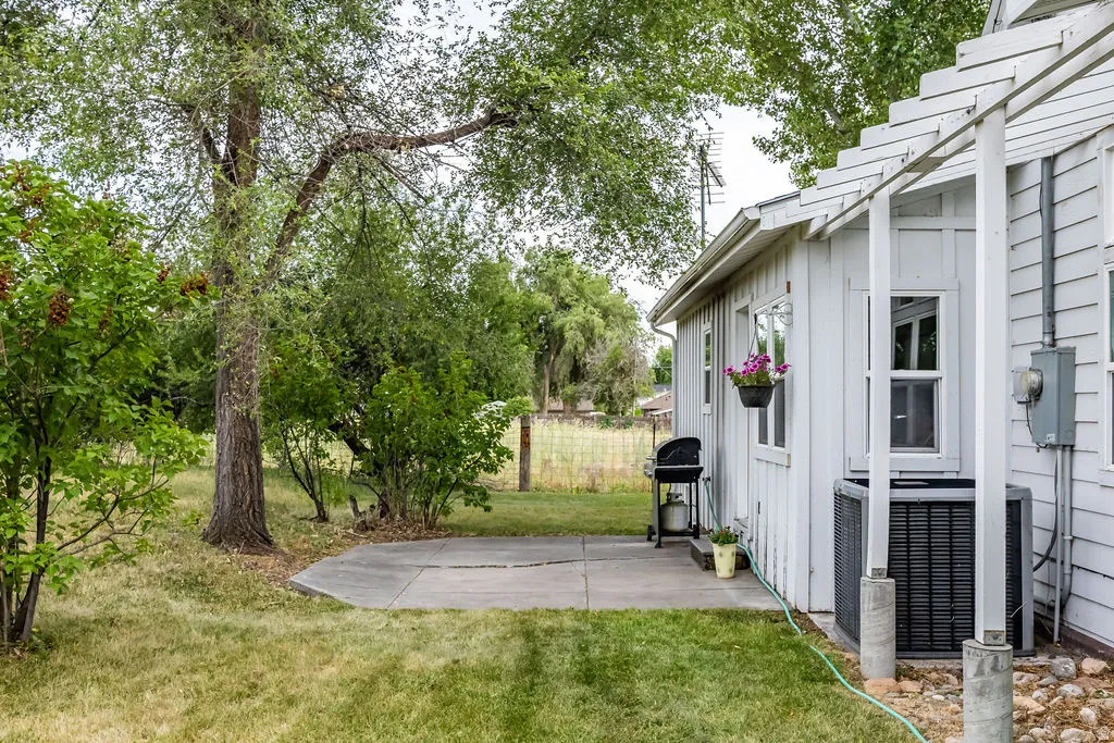 Concrete patio area featuring a white board-and-batten exterior, mature trees, and established shrubbery